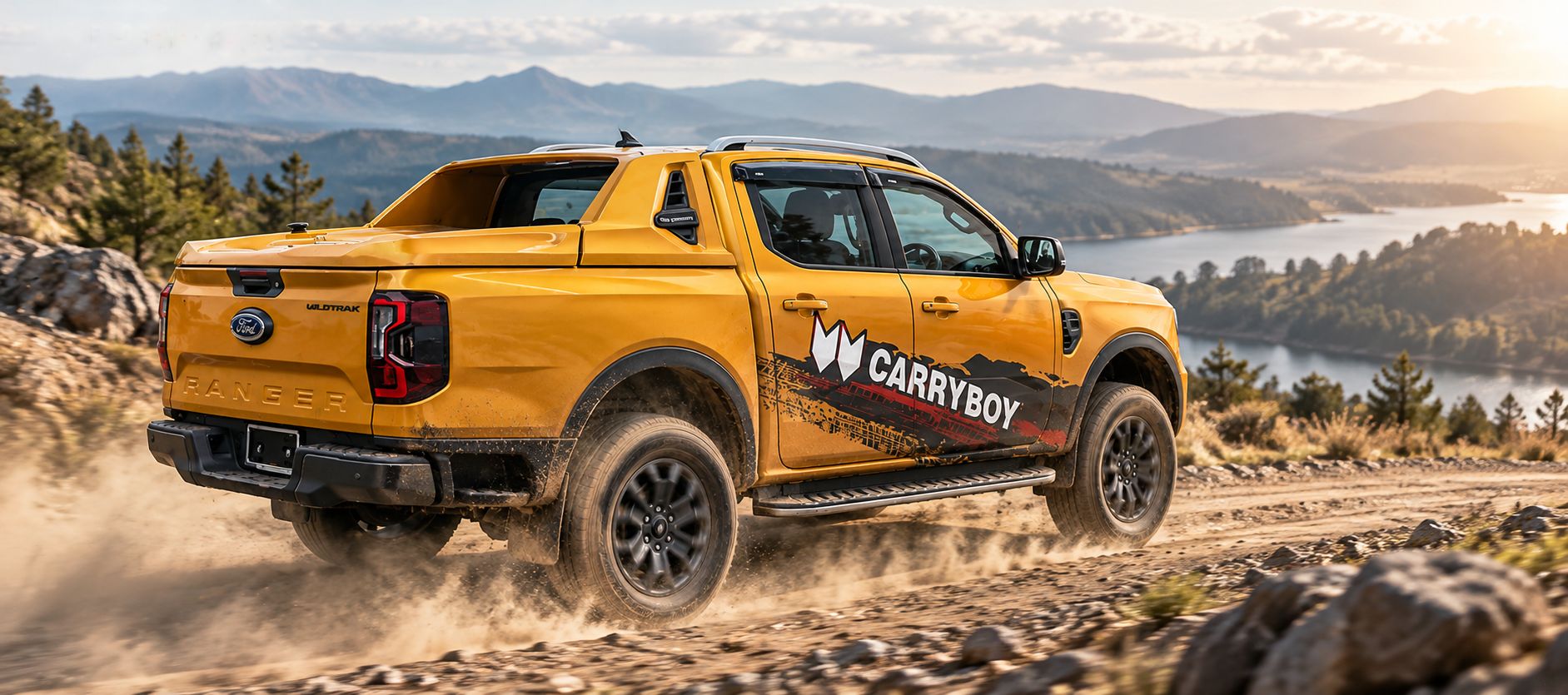 Yellow Ford Ranger Wildtrak fitted with the CARRYBOY CB-762X Full Box, driving up a dusty mountain track above a lake